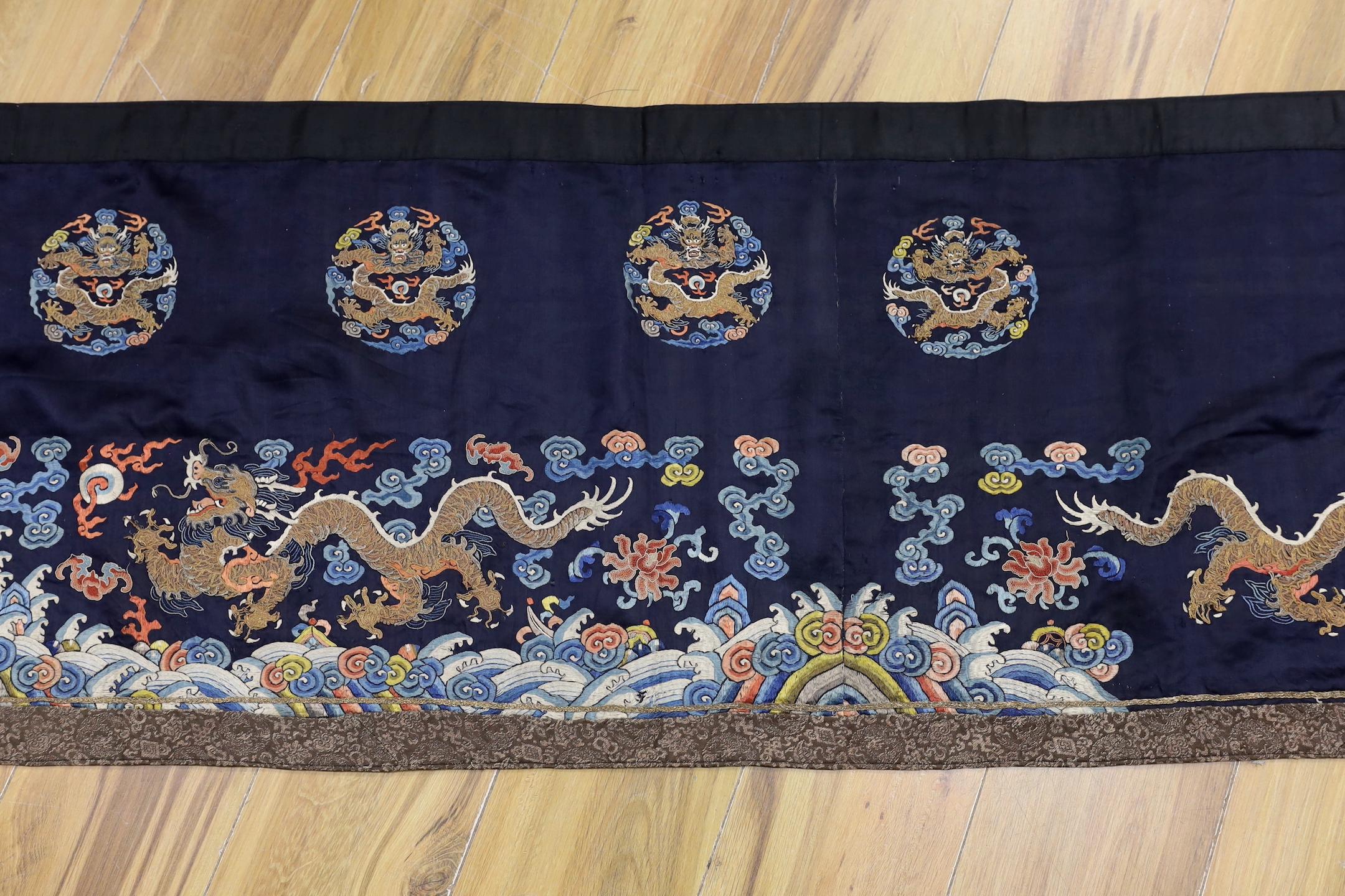A Chinese long dark blue ground ‘dragon’ altar cloth, late Qing dynasty, polychrome embroidered, celestial dragons and mons amongst stylised clouds, 300 x 50cm